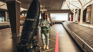 Thrilled man at Tahiti's airport, sporting the Roark Gonzo Camp Collar Shirt - Hinano Otemanu Light Blue with confidence, holding a surfboard travel bag against the backdrop of a empty airport setting.