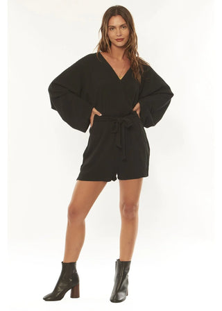 Woman in breezy Fae Woven Romper, Washed Black, showcasing flowy sleeves and tie waist.