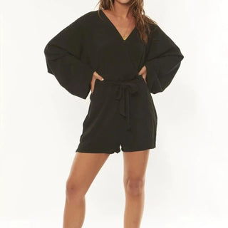 Woman in breezy Fae Woven Romper, Washed Black, showcasing flowy sleeves and tie waist.