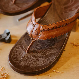 OluKai Hiapo Men's Leather Sandals in Rum/Dark Wood — naturally tumbled marbled full-grain leather with Polynesian whipstitching, moko tattoo footbed, leather-wrapped outsole, and non-marking rubber traction pods