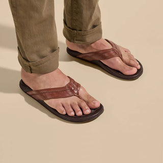 OluKai Hiapo Men's Leather Sandals in Rum/Dark Wood — naturally tumbled marbled full-grain leather with Polynesian whipstitching, moko tattoo footbed, leather-wrapped outsole, and non-marking rubber traction pods