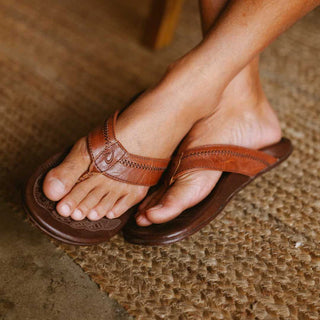 OluKai Hiapo Men's Leather Sandals in Rum/Dark Wood — naturally tumbled marbled full-grain leather with Polynesian whipstitching, moko tattoo footbed, leather-wrapped outsole, and non-marking rubber traction pods