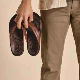 OluKai Hiapo Men's Leather Sandals in Rum/Dark Wood — naturally tumbled marbled full-grain leather with Polynesian whipstitching, moko tattoo footbed, leather-wrapped outsole, and non-marking rubber traction pods