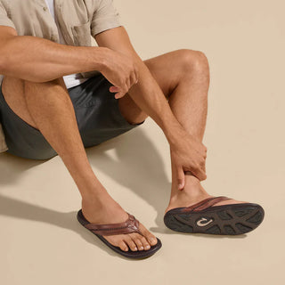 Olukai Mea Ola leather sandals in Tan and Dark Java with whipstitched straps and laser-etched footbed artwork.