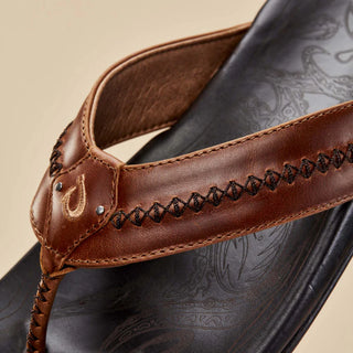 Olukai Mea Ola leather sandals in Tan and Dark Java with whipstitched straps and laser-etched footbed artwork.