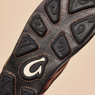 Olukai Mea Ola leather sandals in Tan and Dark Java with whipstitched straps and laser-etched footbed artwork.