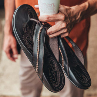 OluKai Mea Ola Leather Sandals in Dark Java/Dark Java — premium full-grain leather with canoe lash whipstitching, octopus laser-etched footbed, microfiber lining, and handsewn leather toe post