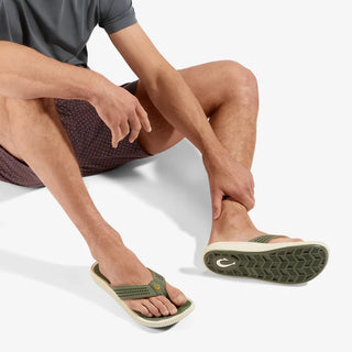Side view of an OluKai Ulele sandal in Shadow Green with laser-cut straps, mustard-colored lining, and a textured cream sole.