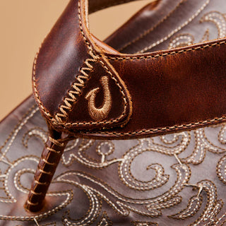 Side view of an OluKai Mekila sandal in Natural/Natural with brown leather straps, stitched edges, and decorative artwork across the footbed.