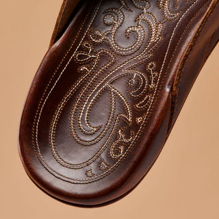 Side view of an OluKai Mekila sandal in Natural/Natural with brown leather straps, stitched edges, and decorative artwork across the footbed.