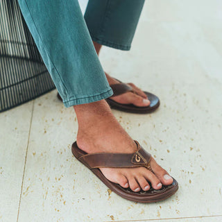 Side view of an OluKai Mekila sandal in Natural/Natural with brown leather straps, stitched edges, and decorative artwork across the footbed.
