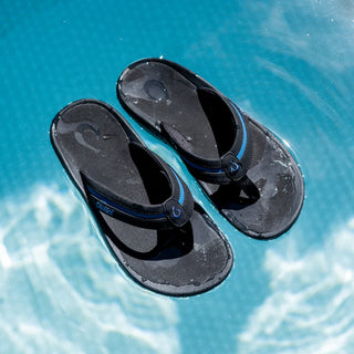 OluKai 'Ohana Pālua Men's Beach Sandals in Black/Slate Blue, synthetic split strap with jersey knit lining, signature 'Ohana compression-molded EVA footbed, and non-marking rubber coral-inspired lug outsole