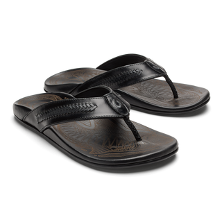 OluKai Mea Ola Mano Sandals in Black/Dark Shadow — premium full-grain leather with hand-woven Polynesian lashing details, laser-etched Mano shark artwork, flexible midsole, and cushioned footbed