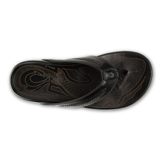 OluKai Mea Ola Mano Sandals in Black/Dark Shadow — premium full-grain leather with hand-woven Polynesian lashing details, laser-etched Mano shark artwork, flexible midsole, and cushioned footbed