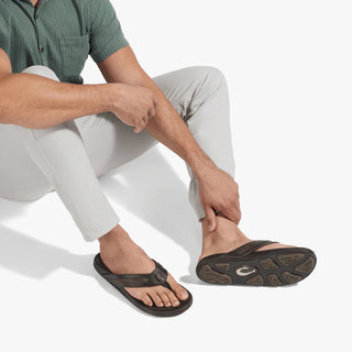 OluKai Mea Ola Mano leather sandals in Dark Java/Mustang with woven straps and shark-inspired etched detailing.