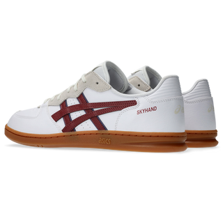 ASICS SKYHAND OG sneaker in white and brisket red with suede paneling, gum outsole, and retro handball-inspired design.