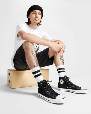 Person wearing black high-top sneakers with white stripes, sitting on a wooden box against a plain background.