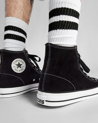 Black Converse All Star high-top sneakers with white soles worn with striped socks on a light gray background.