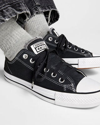 Black Converse sneakers worn with gray socks on a light gray background