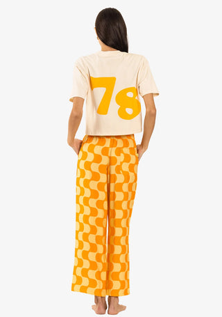 A woman wearing Duvin's Golden Hour Pants with relaxed fitting cabana style, made from a blend of 58% rayon and 42% polyester, featuring a wide-leg cropped style, adjustable drawstring, single back pocket, and a side hem woven label.