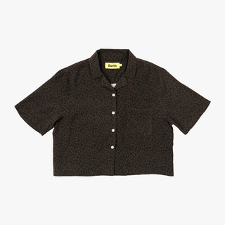 A woman in a Duvin Black Leopard Button-up Shirt with a relaxed, cropped cabana fit, made from a blend of 58% rayon and 42% polyester, featuring a camp collar, black leopard print, and side hem woven label.