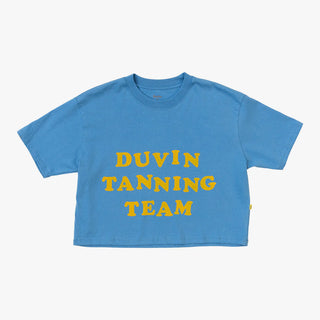A woman in a Duvin 'Tanning Team' Crop Tee in blue, made from 100% high-quality Peruvian Pima Cotton, flaunting a cropped boxy fit, custom dyed color, anti-pilling, pre-shrunk, and a Duvin-branded yellow woven side-seam label.