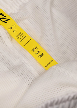 Close-up of a yellow tag on a white swim short with branding details.