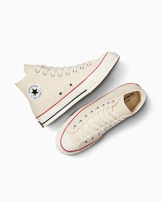 Pair of beige high-top sneakers with red accents on a white background