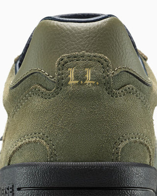 Close-up of a green suede shoe with a brand logo on a white background