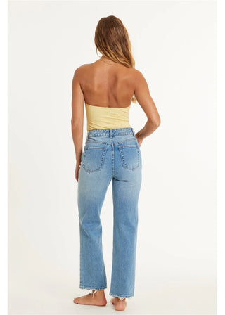 Woman wearing light blue jeans and a yellow top on a white background