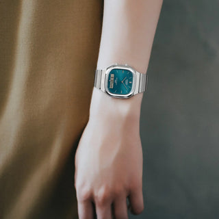 Wrist wearing a silver watch with a blue face against a blurred background