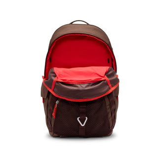 Close-up of the brown Nike ACG DAYMAX Backpack showing mesh paneling, adjustable webbing straps, buckle closures, and a red zipper pull