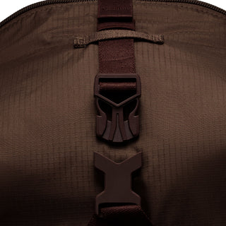 Close-up of the brown Nike ACG DAYMAX Backpack showing mesh paneling, adjustable webbing straps, buckle closures, and a red zipper pull