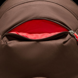 Close-up of the brown Nike ACG DAYMAX Backpack showing mesh paneling, adjustable webbing straps, buckle closures, and a red zipper pull