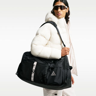 Nike ACG DAYMAX Duffel Bag in Black/College Grey with black carry handles, grey webbing straps, a front zippered pocket, and a small ACG logo