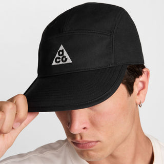 black Nike ACG Fly Unstructured Cap with a white embroidered ACG logo, holding the front of the bill.