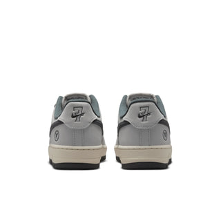 A pair of low-top sneakers shown from the back, featuring a light gray leather upper, dark gray overlays with a stylized '7' logo, a cream midsole, and a black outsole.