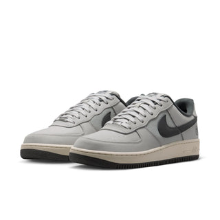 A pair of Nike Air Force 1 Low sneakers in a light gray colorway, featuring a light gray leather and mesh upper, dark gray Swooshes, a cream midsole, and a black outsole, shown against a plain white background.