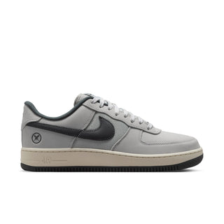 A Nike Air Force 1 Low sneaker in a light gray and dark gray colorway, featuring a light gray leather upper, dark gray Swoosh and heel tab, a beige midsole, and a black outsole.