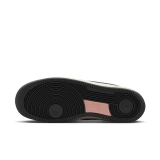 The outsole of a Nike Air Force 1 sneaker, showing a black treaded rubber bottom with a light pink Nike logo patch in the center, photographed on a white background.