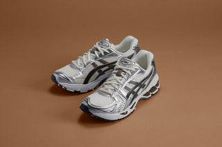 The ASICS GEL-KAYANO® 14 Cream/Black running shoe, sold at Drift House, features a 2000s-inspired design with a layered leather and mesh construction. The midsole is embedded with GEL® technology for shock absorption and Trusstic System® technology for a lightweight feel.
