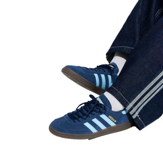 Blue Adidas sneakers with white stripes worn with dark jeans on a white background
