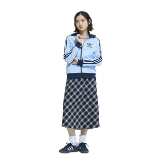 Person wearing a light blue Adidas tracksuit with a dark blue skirt on a white background
