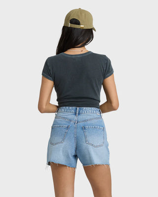 Person wearing a dark gray t-shirt, light blue denim shorts, and a beige cap on a white background