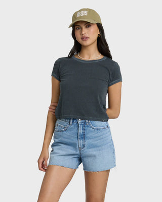 Woman wearing a dark gray t-shirt and light blue shorts with a beige cap on a white background