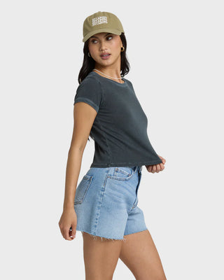 Woman wearing a dark gray t-shirt, light blue denim shorts, and a beige cap on a white background