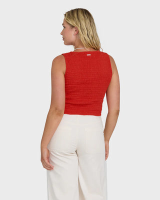 Woman wearing a red sleeveless top and white pants on a white background