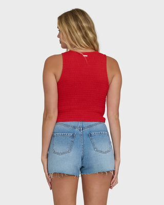 Woman wearing a red sleeveless top and denim shorts on a white background