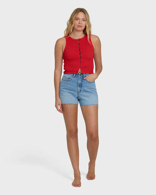 Woman wearing a red sleeveless top and blue denim shorts on a white background