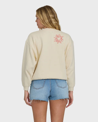 Woman wearing a beige sweatshirt with a red sun design on the back, standing against a plain background.